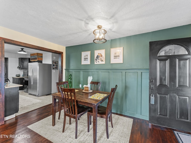 dining space with a textured ceiling, an inviting chandelier, wood finished floors, and a decorative wall