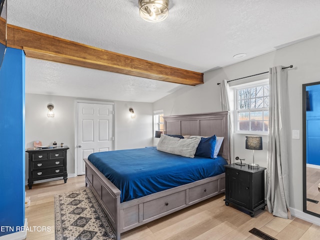 bedroom featuring visible vents, beamed ceiling, a textured ceiling, and light wood-style floors