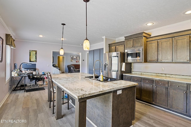 kitchen with crown molding, an island with sink, light wood-style floors, hanging light fixtures, and stainless steel appliances