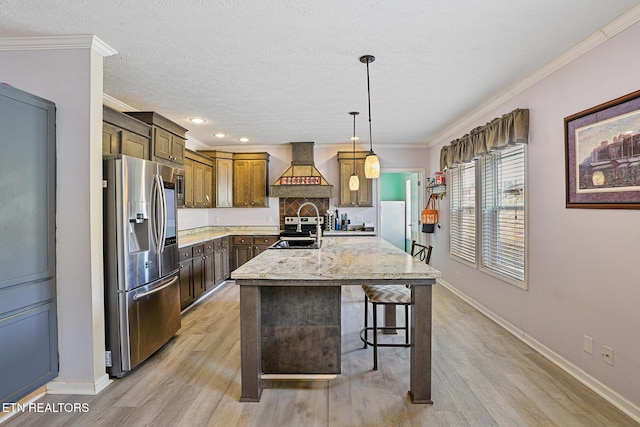 kitchen featuring light wood-type flooring, an island with sink, ornamental molding, custom exhaust hood, and stainless steel appliances