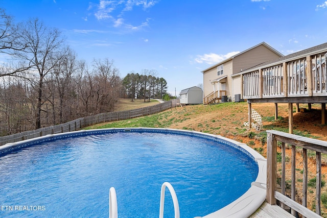 view of pool featuring a fenced in pool, a wooden deck, a storage shed, a fenced backyard, and an outdoor structure