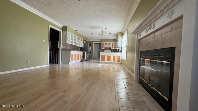 unfurnished living room with light wood finished floors, a notable chandelier, a textured ceiling, and ornamental molding