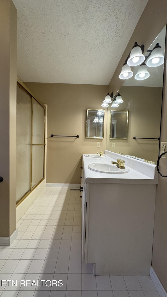 full bath featuring a sink, a textured ceiling, a shower stall, tile patterned flooring, and double vanity