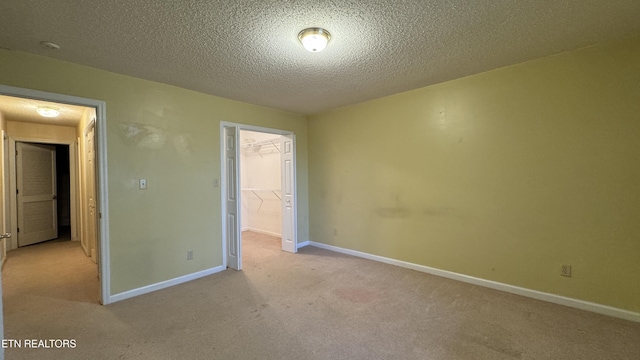 unfurnished bedroom with a walk in closet, carpet, baseboards, a closet, and a textured ceiling