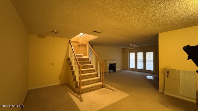 stairs featuring visible vents, a ceiling fan, a textured ceiling, carpet floors, and a fireplace