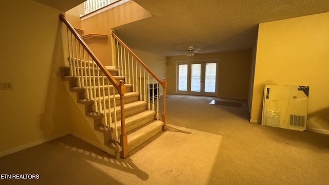 staircase featuring visible vents, a textured ceiling, carpet floors, baseboards, and ceiling fan