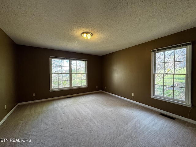 carpeted spare room featuring baseboards, visible vents, and a textured ceiling