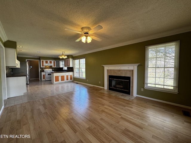 unfurnished living room with a tiled fireplace, ornamental molding, ceiling fan with notable chandelier, and wood finished floors