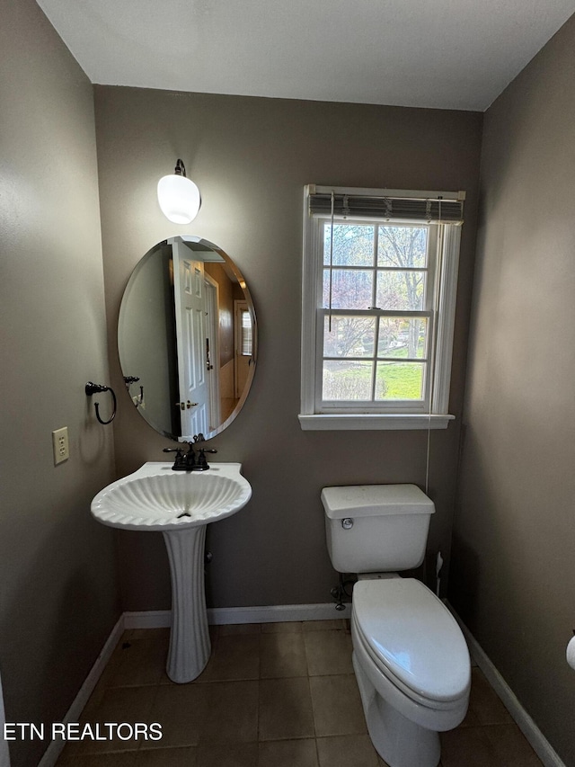 half bathroom with baseboards, toilet, and tile patterned floors