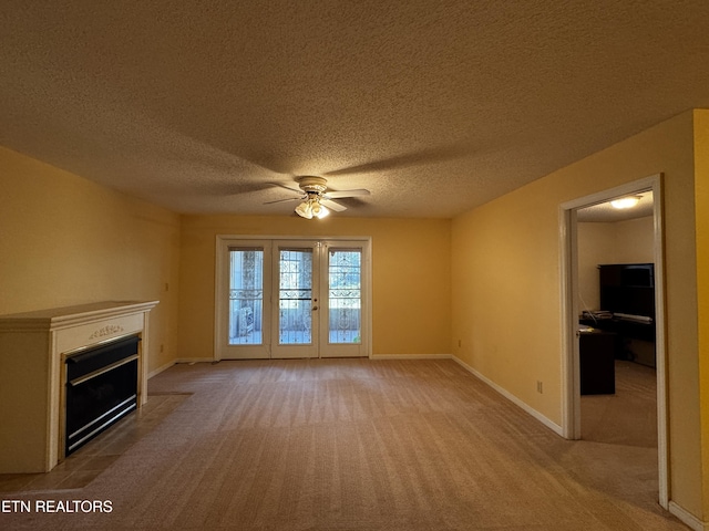 unfurnished living room featuring a fireplace with flush hearth, a textured ceiling, baseboards, a ceiling fan, and light colored carpet