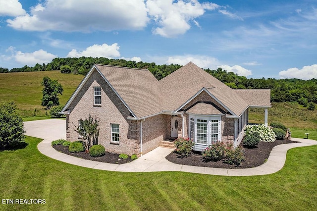 view of front of home featuring a front yard, brick siding, and roof with shingles