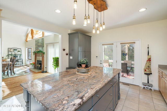 kitchen with gray cabinets, a kitchen island, a fireplace, light stone countertops, and hanging light fixtures