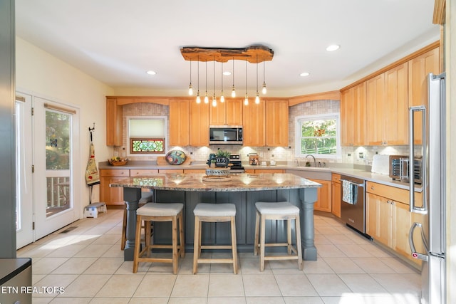 kitchen with light stone counters, a center island, stainless steel appliances, light tile patterned flooring, and decorative backsplash