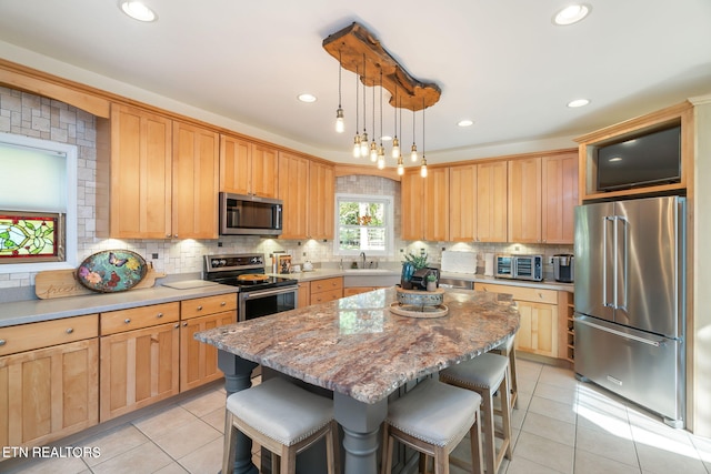 kitchen with light tile patterned floors, a kitchen island, stainless steel appliances, a kitchen bar, and backsplash