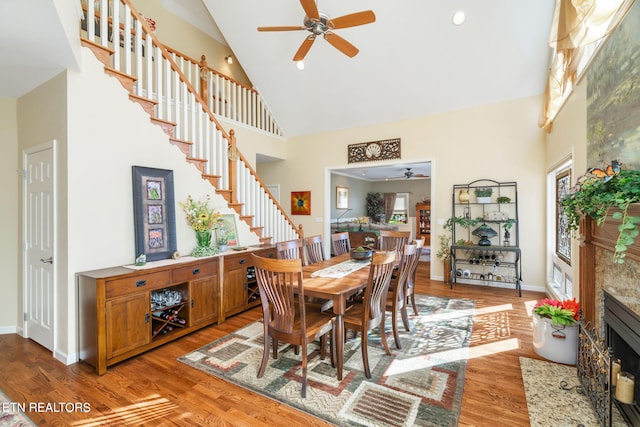 dining space with baseboards, high vaulted ceiling, a tile fireplace, stairs, and light wood-type flooring