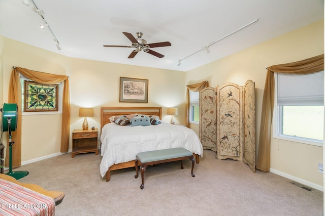 carpeted bedroom featuring track lighting, a ceiling fan, visible vents, and baseboards