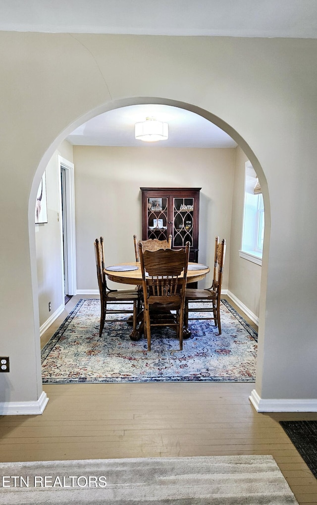 dining room featuring baseboards, arched walkways, and wood-type flooring