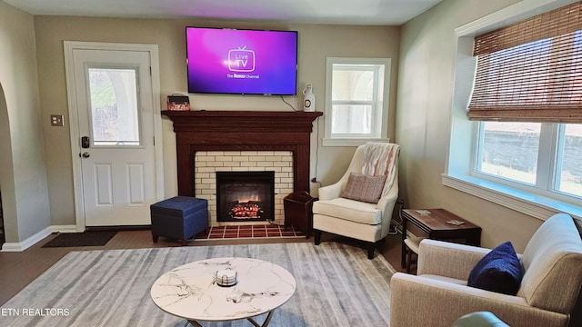 sitting room with plenty of natural light, a brick fireplace, baseboards, and wood finished floors