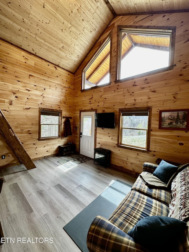 unfurnished living room with high vaulted ceiling, a healthy amount of sunlight, wood finished floors, and wood walls