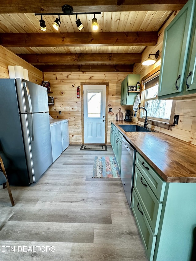 kitchen with wood walls, stainless steel appliances, green cabinets, and a sink