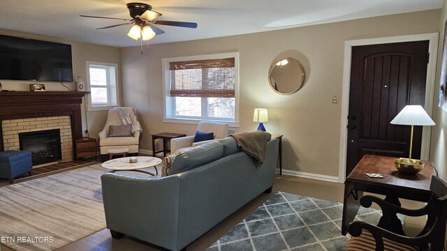 living area featuring baseboards, a ceiling fan, wood finished floors, and a fireplace