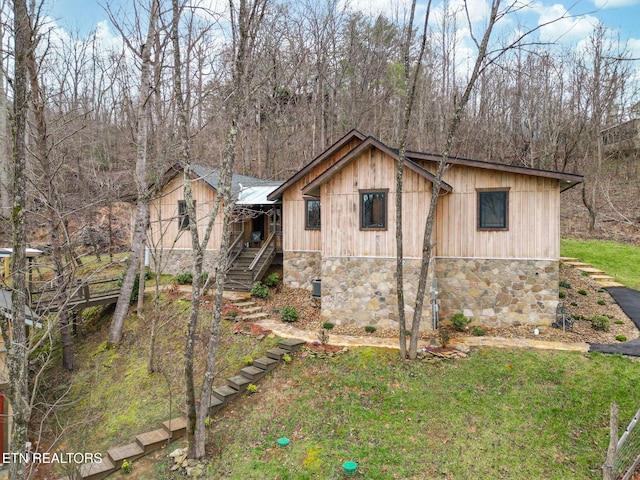 view of front of property with stone siding, a lawn, and stairway