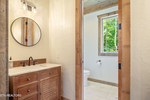 bathroom with baseboards, toilet, vanity, and a textured wall