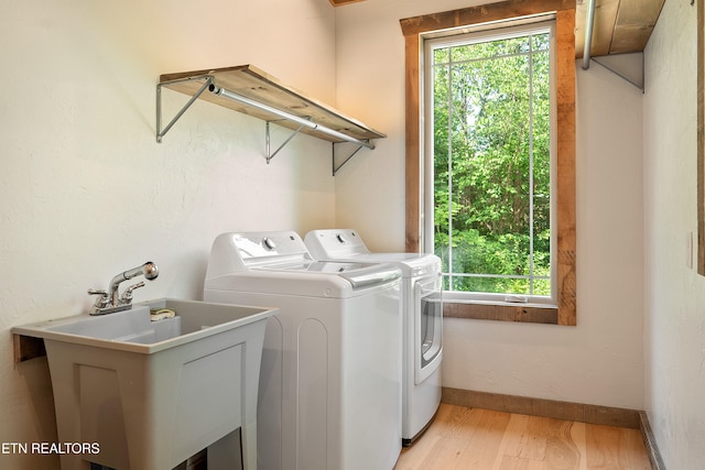 clothes washing area with light wood-style flooring, a sink, separate washer and dryer, baseboards, and laundry area