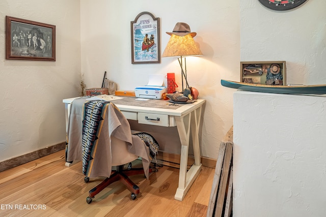 office area featuring a baseboard heating unit, light wood-style flooring, a textured wall, and baseboards