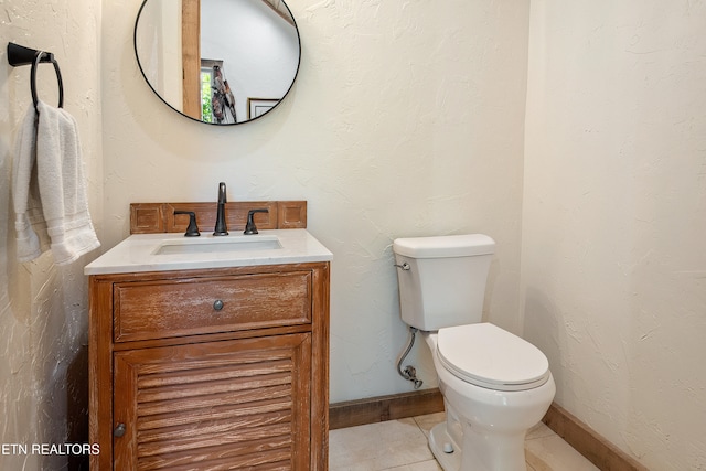 bathroom featuring tile patterned flooring, baseboards, toilet, a textured wall, and vanity