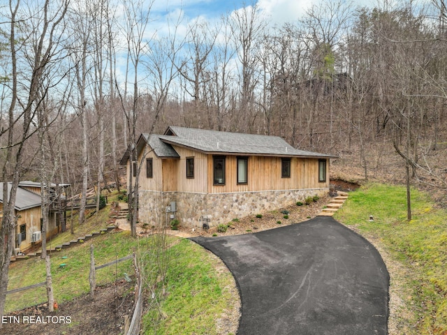 view of front of property featuring stone siding, stairway, driveway, and a front lawn