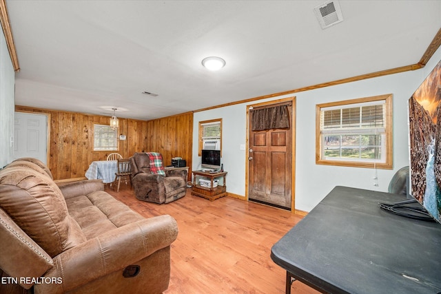 living area with light wood-type flooring, visible vents, baseboards, and crown molding