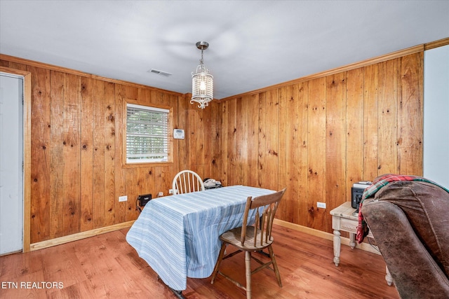 dining area with visible vents, baseboards, wooden walls, and wood finished floors