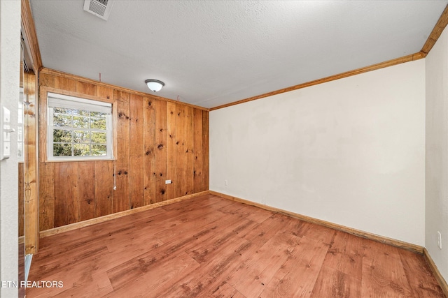 empty room featuring visible vents, crown molding, baseboards, wood walls, and wood finished floors