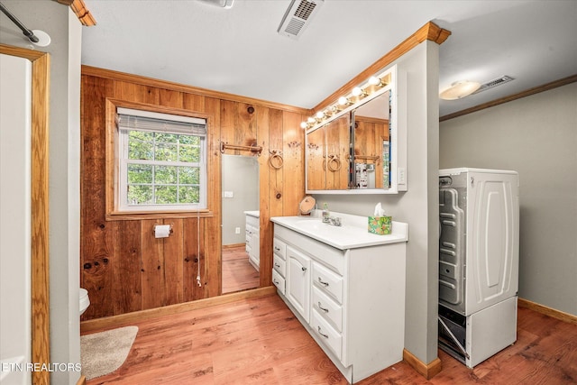 full bath with vanity, wooden walls, wood finished floors, visible vents, and washer / dryer