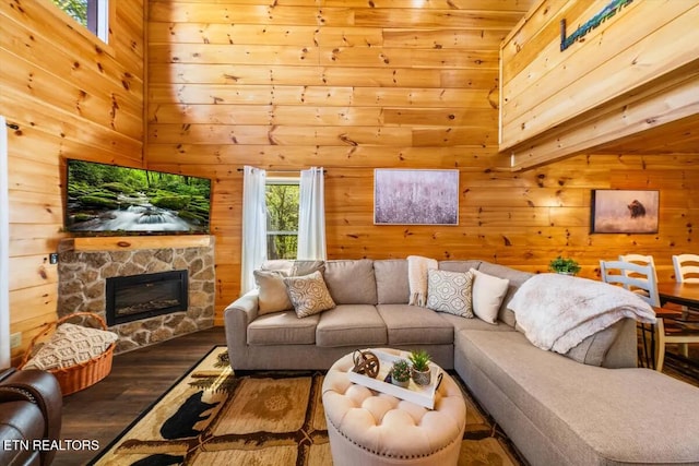 living area with wooden walls, a stone fireplace, wood finished floors, and a towering ceiling