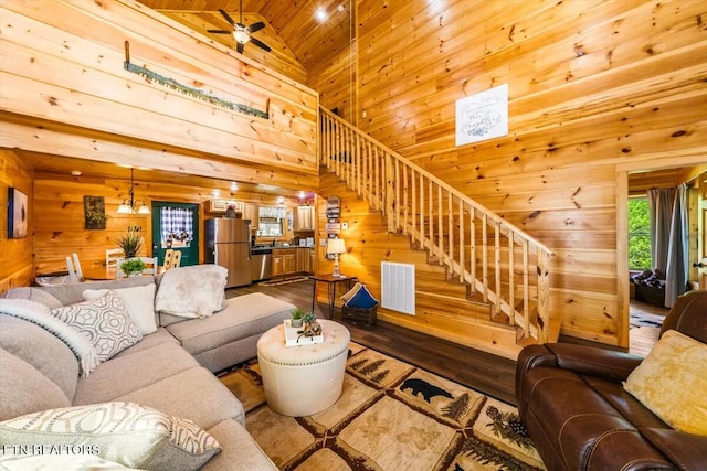 living area featuring wooden walls, dark wood-style floors, visible vents, high vaulted ceiling, and stairs