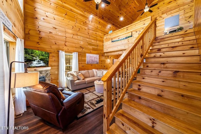 living area with stairway, wooden walls, wood finished floors, high vaulted ceiling, and ceiling fan