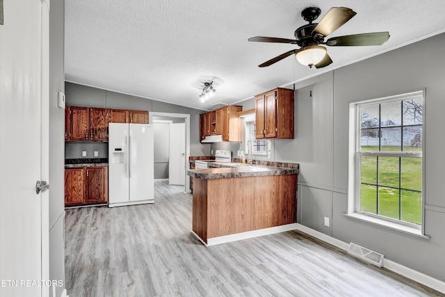 kitchen featuring dark countertops, visible vents, lofted ceiling, a peninsula, and white appliances