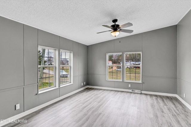 unfurnished room featuring visible vents, a ceiling fan, a textured ceiling, wood finished floors, and a decorative wall