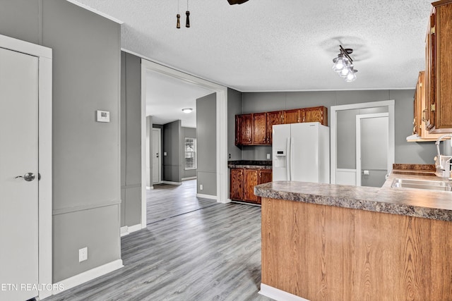 kitchen featuring brown cabinets, a sink, wood finished floors, white fridge with ice dispenser, and a peninsula