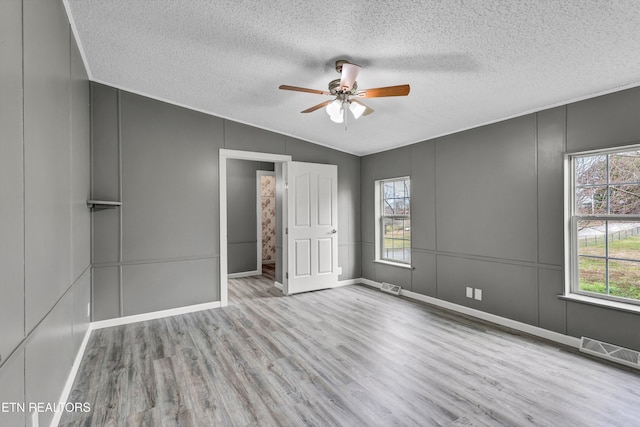 unfurnished bedroom featuring vaulted ceiling, a decorative wall, wood finished floors, and visible vents