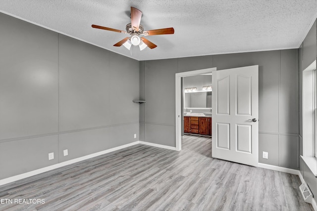 unfurnished bedroom with visible vents, a textured ceiling, wood finished floors, a decorative wall, and ceiling fan