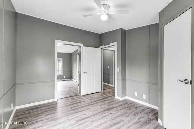 unfurnished bedroom with wood finished floors, baseboards, ceiling fan, a textured ceiling, and a decorative wall