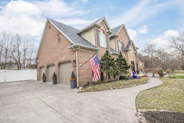 view of side of property with concrete driveway, fence, brick siding, and a shingled roof