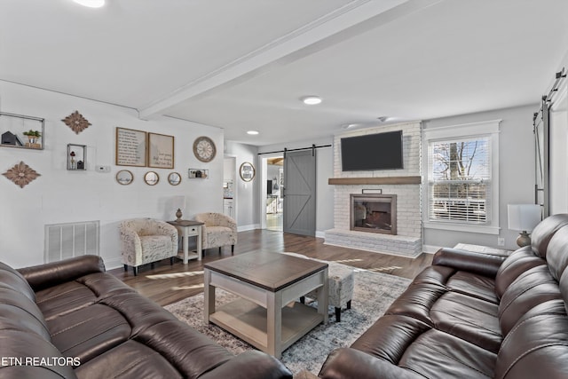 living area featuring a barn door, beam ceiling, visible vents, and wood finished floors