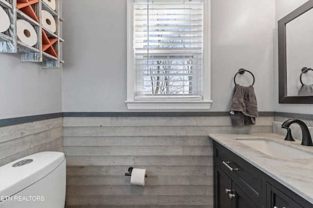 half bathroom featuring a wainscoted wall, toilet, and vanity