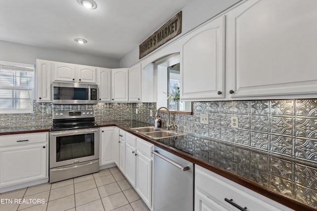 kitchen with a sink, tasteful backsplash, white cabinetry, appliances with stainless steel finishes, and light tile patterned floors