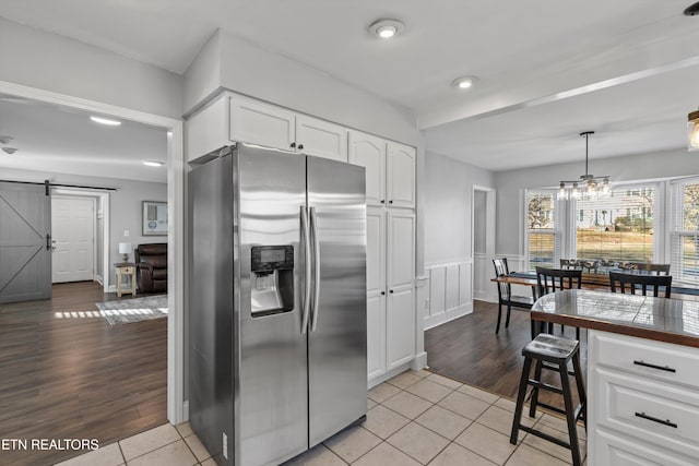 kitchen with a wainscoted wall, white cabinetry, a barn door, stainless steel fridge, and light tile patterned floors