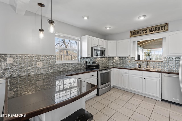 kitchen with a sink, decorative light fixtures, stainless steel appliances, white cabinets, and decorative backsplash